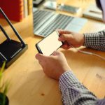 Środkowa sekcja mężczyzny używającego smartfonu siedząc przy biurku w biurze