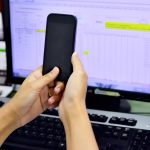 Przycięty obraz kobiety trzymającej telefon komórkowy przy komputerze