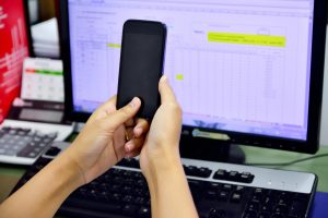 Przycięty obraz kobiety trzymającej telefon komórkowy przy komputerze