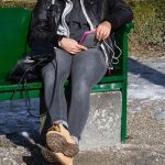 Dolna część kobiety używającej telefonu komórkowego podczas siedzenia na ławce w zimie