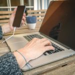 Środkowa sekcja kobiety używającej telefonu komórkowego i laptopa na stole