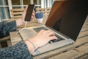 Środkowa sekcja kobiety używającej telefonu komórkowego i laptopa na stole