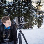 Dojrzały mężczyzna z plecakiem i statywem stojący na śniegu