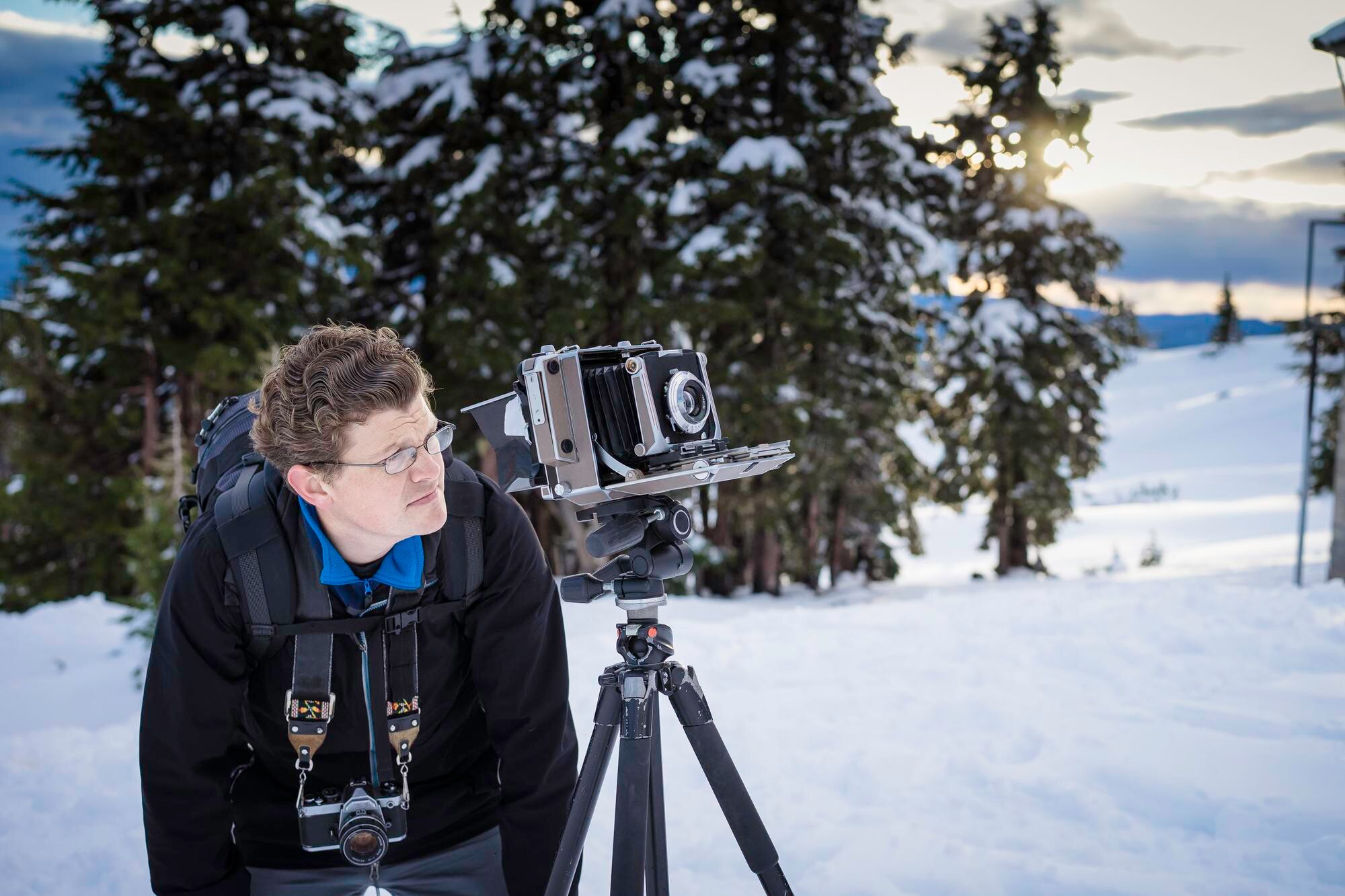 Dojrzały mężczyzna z plecakiem i statywem stojący na śniegu