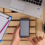 Odcięta ręka bizneswoman używającej smartfona, siedząc w biurze.