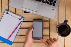 Odcięta ręka bizneswoman używającej smartfona, siedząc w biurze.