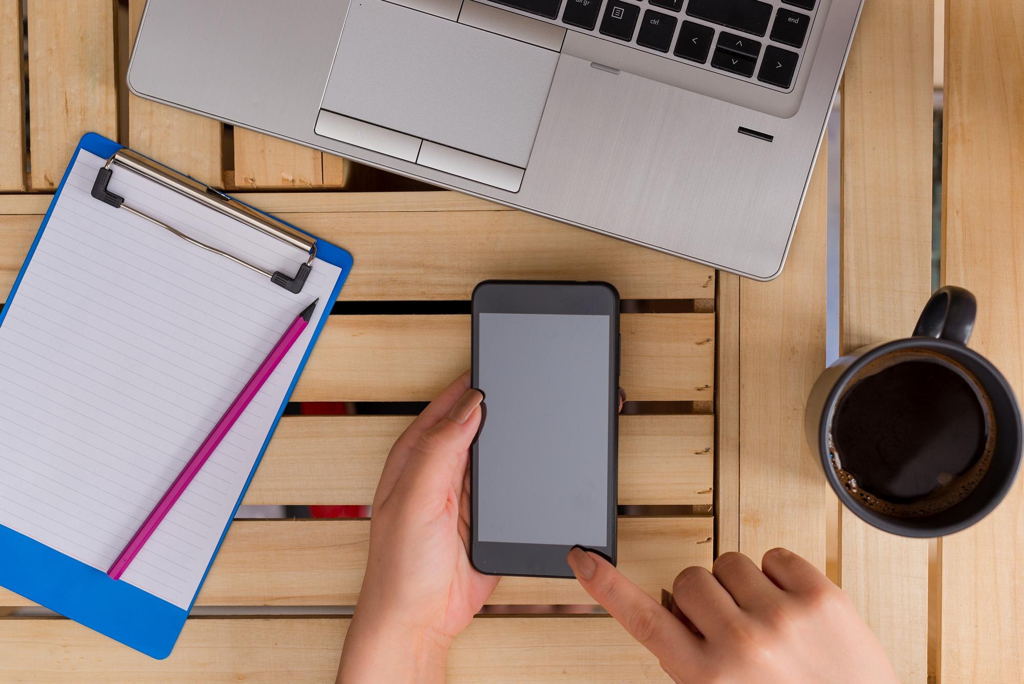 Odcięta ręka bizneswoman używającej smartfona, siedząc w biurze.