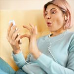 Zaskoczona młoda kobieta przewijająca wiadomości za pośrednictwem konta w mediach społecznościowych, zszokowana.