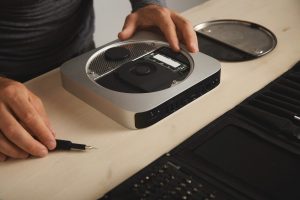 Otwarty komputer osobisty na białym stole w laboratorium naprawy usług elektronicznych, z bliska, mistrz bierze sterownik bitowy