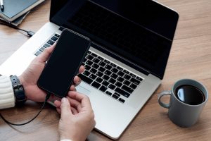 Przycięte zdjęcie ręki człowieka trzymającego smartfon z czarnym ekranem siedząc przy stole