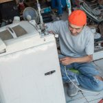 Azjatycki pracownik naprawia zepsute okablowanie pralki