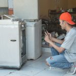 mechanik kuca i robi zdjęcie uszkodzenia pralki za pomocą aparatu w telefonie komórkowym