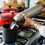 Wycięty obraz starszej kobiety nalewającej wodę do pojemnika na kuchence