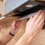 Mężczyzna naprawia okap w kuchni. Filtr wymienny w okapie kuchennym