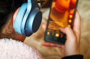 Widok z tyłu nastolatki używającej telefonu komórkowego z słuchawkami