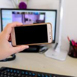 Przycięte ręce osoby używającej telefonu na stole