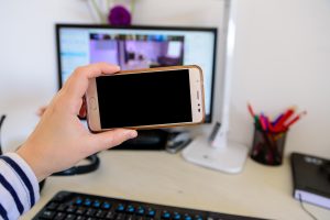 Przycięte ręce osoby używającej telefonu na stole