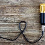 Złoty mikrofon pojemnościowy z kablem leży na drewnianym stole z miejscem na kopię. Motyw muzyczny. Leżał na płasko. Widok z góry.