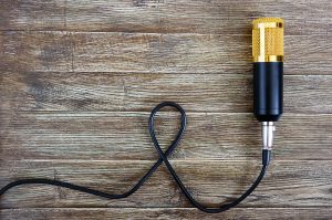 Złoty mikrofon pojemnościowy z kablem leży na drewnianym stole z miejscem na kopię. Motyw muzyczny. Leżał na płasko. Widok z góry.