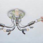 Zastępując lampy w żyrandolu pokojowym, żeńska ręka instaluje kukurydzianą lampę LED w uchwycie lampy.