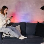 Młoda azjatycka kobieta siedzi na kanapie w przytulnym pokoju patrzy na telefon