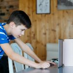 Widok boczny chłopca używającego telefonu komórkowego na stole