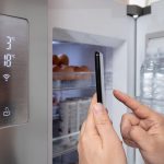 Ręka mężczyzny, który swoim smartfonem steruje lodówką. Koncepcja Internetu rzeczy.