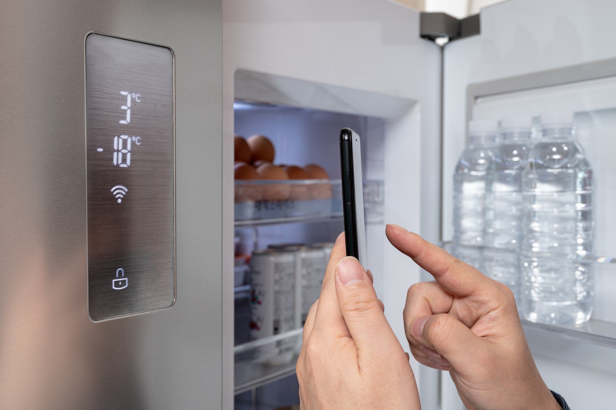 Ręka mężczyzny, który swoim smartfonem steruje lodówką. Koncepcja Internetu rzeczy.