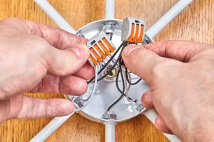 Elektryk montuje okablowanie wewnątrz skrzynki elektrycznej lampy sufitowej za pomocą listwy zaciskowej z dźwigniami.