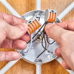 Elektryk montuje okablowanie wewnątrz skrzynki elektrycznej lampy sufitowej za pomocą listwy zaciskowej z dźwigniami.