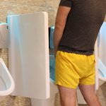 Mężczyzna w żółtej wełnie sika w portrecie toalety publicznej