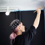 Widok młodej dziewczyny z różowymi włosami, malowanie ścian pędzlem i białym kolorem z tyłu.