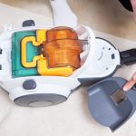 Kobieta wyjmuje pojemnik z kurzem z odkurzacza. Sprzęt AGD