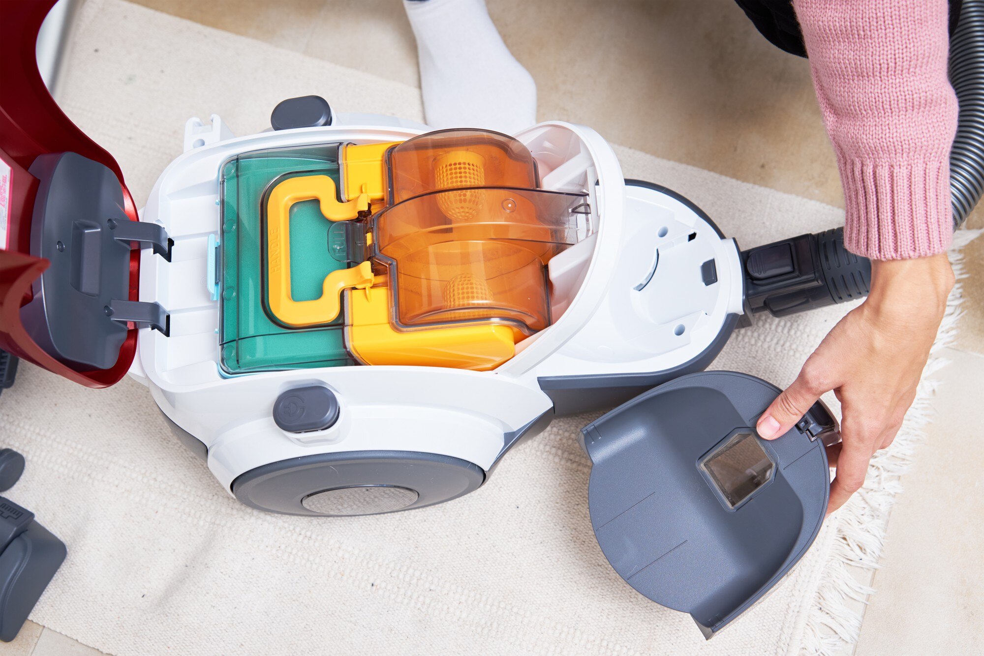 Kobieta wyjmuje pojemnik z kurzem z odkurzacza. Sprzęt AGD