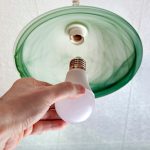 Zbliżenie na energooszczędną żarówkę LED w ludzkiej dłoni, zamiana lampy w oprawie sufitowej z zielonego szlifowanego szkła.