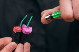 Podpalenie kilku petard. Mężczyzna w czarnych szatach zapala jednocześnie dwa petardy.