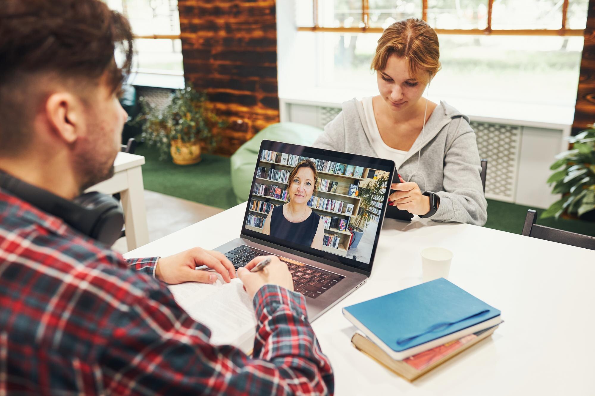Studenci uczący się w bibliotece uniwersyteckiej młody człowiek mający zajęcia wideo na laptopie wraca do szkoły