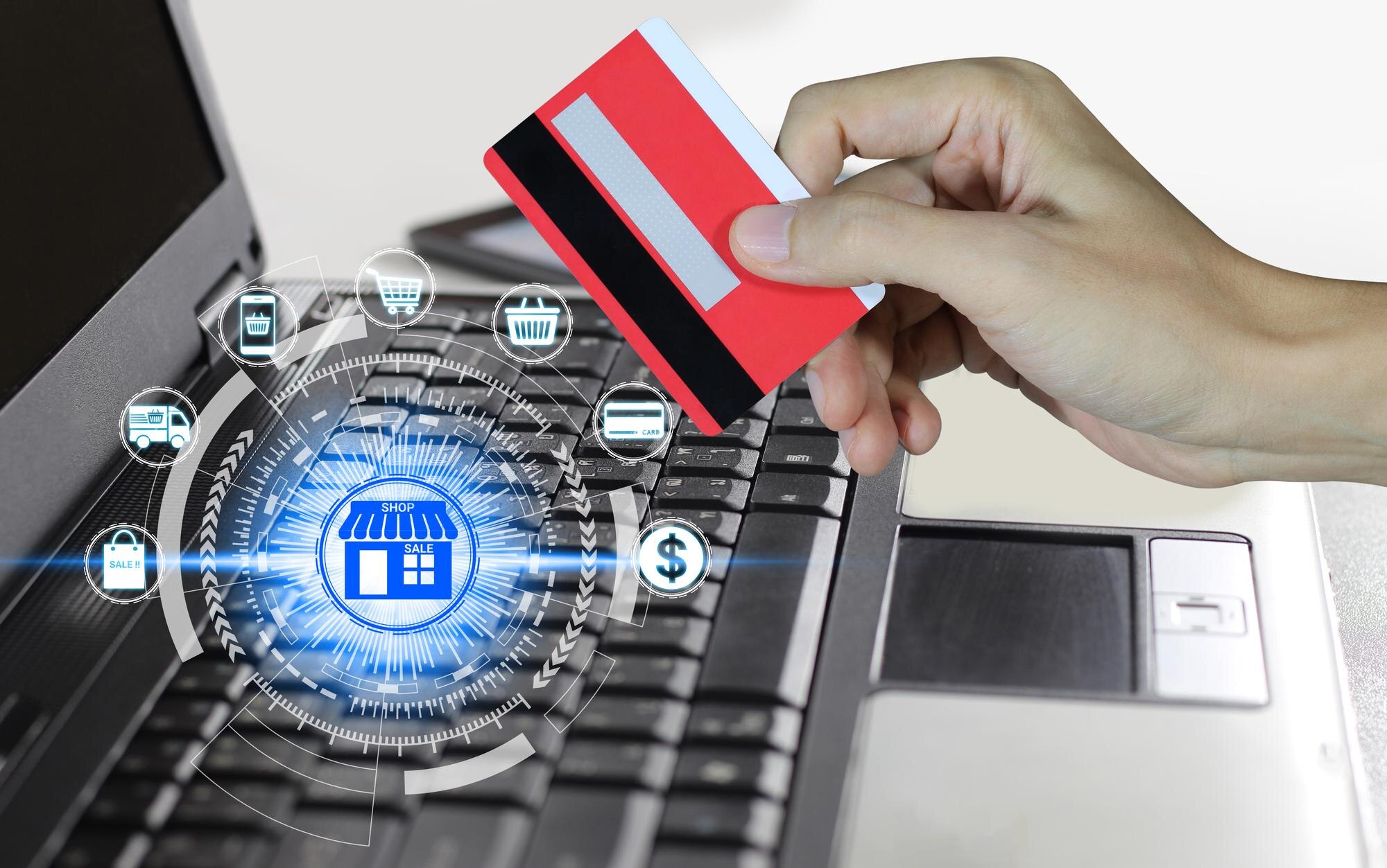 Cyfrowy kompozytowy obraz przyciętej ręki trzymającej kartę kredytową przez laptop na stole