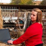 Młoda kobieta używająca laptopa na balie siana na farmie