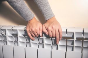 Kobieta ogrzewa ręce w pobliżu grzejnika w domu po spacerze