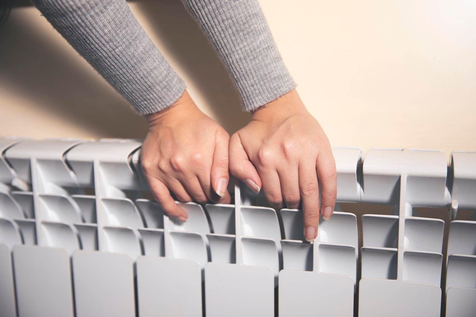 Kobieta ogrzewa ręce w pobliżu grzejnika w domu po spacerze