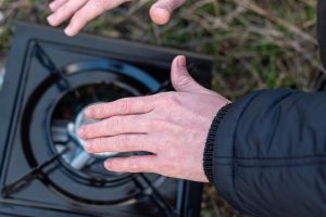 Indywidualny podróżnik zapala piec turystyczny i ogrzewa dłonie podczas górskiej wędrówki