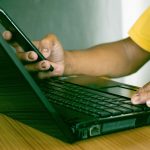 Mężczyzna używający smartfonu komórkowego pracujący w domu z komputerem