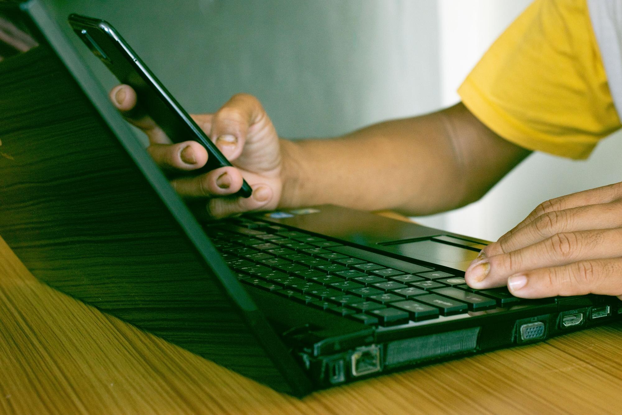 Mężczyzna używający smartfonu komórkowego pracujący w domu z komputerem