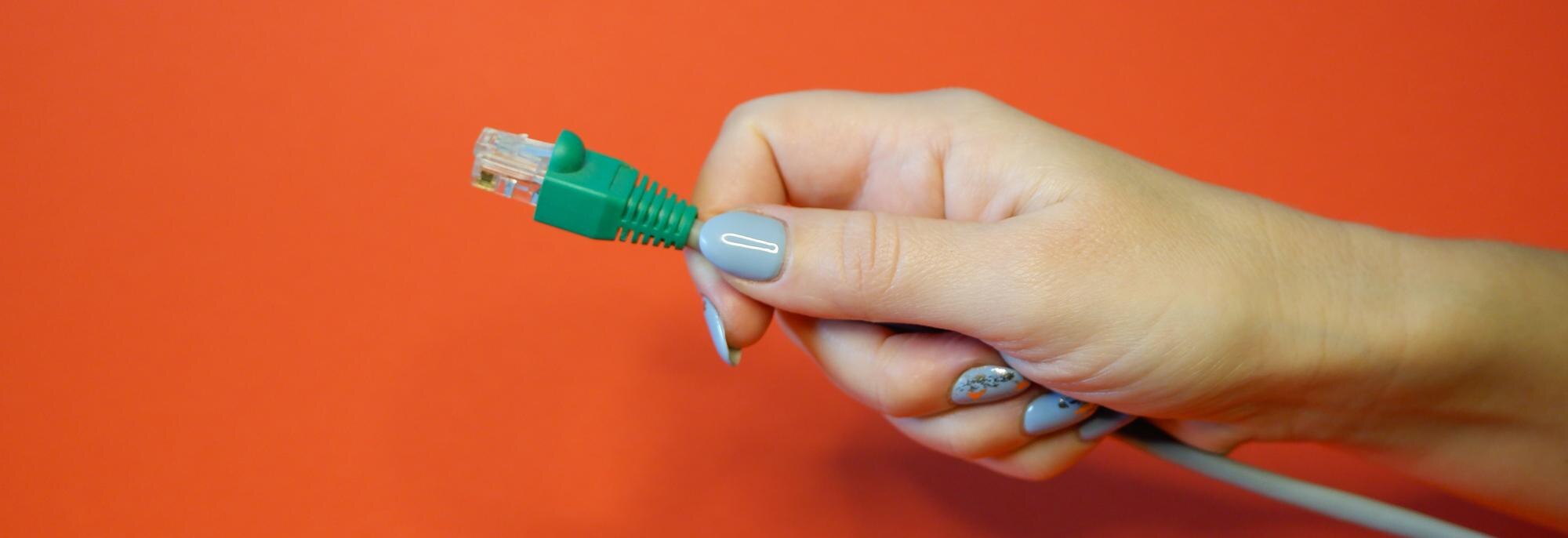 Zielony konektor sieciowy RJ45 na czerwonym tle w zadbanych rękach kobiet