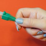 Zielony konektor sieciowy RJ45 na czerwonym tle w zadbanych rękach kobiet