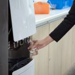 Kobieta ręka trzyma szklankę napełniania chłodną wodą z dystrybutora wody