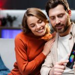 Uśmiechnięta piękna para atrakcyjny mężczyzna i kobieta trzymający telefon komórkowy wskazujący palcem na ekran