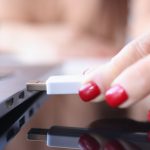 Ręka kobiety wkłada pamięć flash USB do złącza laptopa