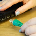 Ręka kobiety łączy konektor sieciowy RJ45 z laptopem